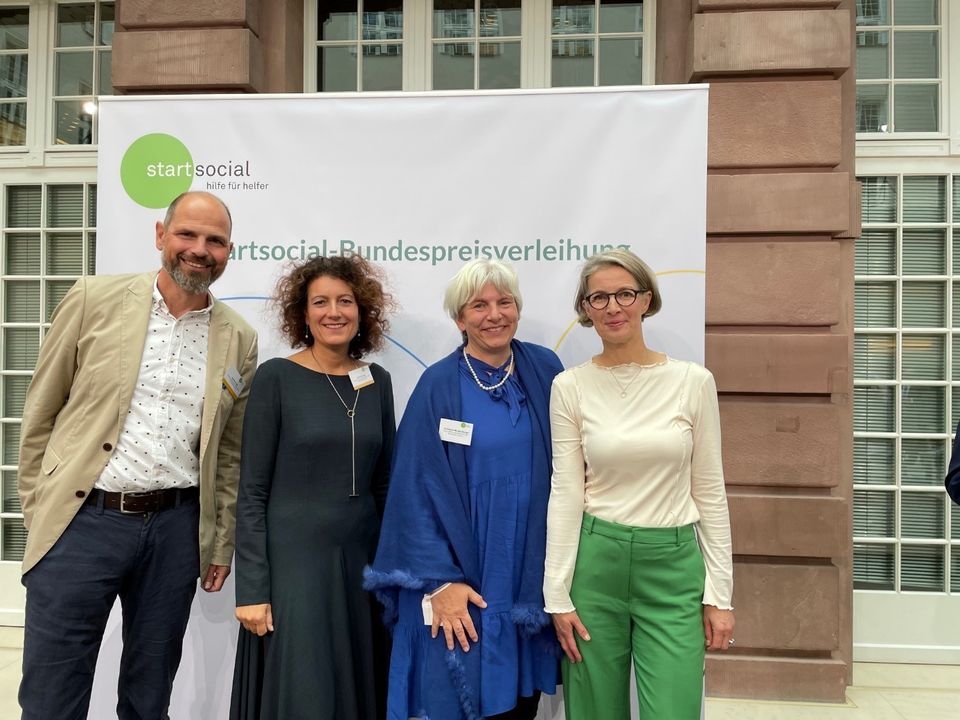 Vier Personen stehen nebeneinander vor einer startsocial-Stellwand.